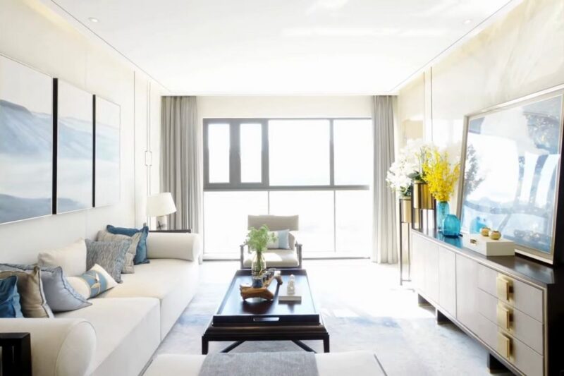 Moderan dnevni boravak sa belom ugaonom garniturom, plavim jastucima, crnim stočićem i TV komodom uz prozore